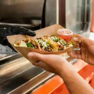 Tacos, a paper tray of fresh street tacos handed across a taco truck serving window